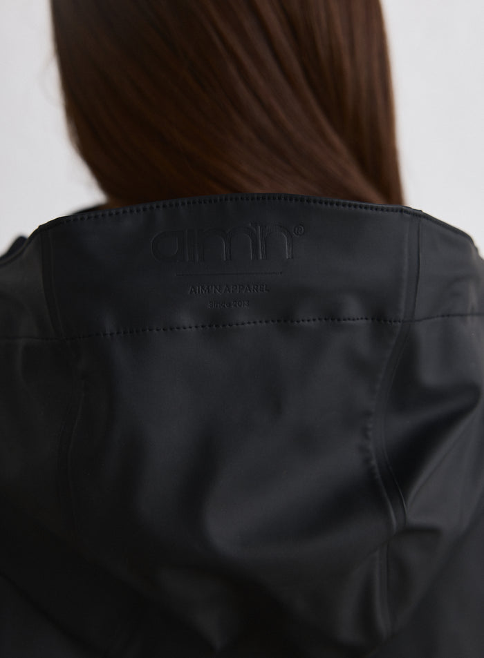 Lähikuva mustan Rain Jacket -sadetakin yläselästä, jossa on sävy sävyyn oleva aim'n-logo [M-174cm]