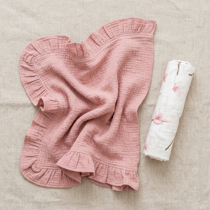 Pink ruffled blanket and a rolled-up swaddle with floral patterns on a beige surface