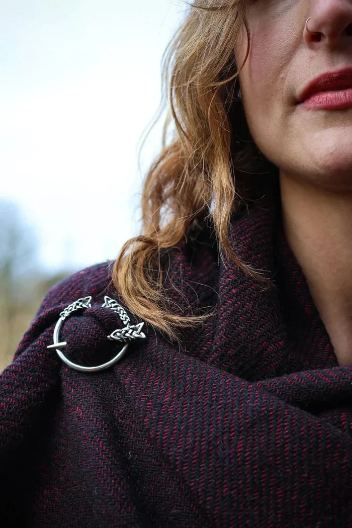 Close up of silver plated Celtic penannular brooch with Trinity knot detail fastening a burgundy shawl
