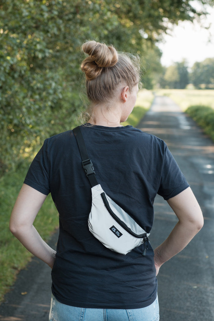 Ela Mo™ Hipbag  | Reflective. Eine Frau mit Hipbag an einem sonnigen Tag auf der Wiese, Ansicht von hinten.