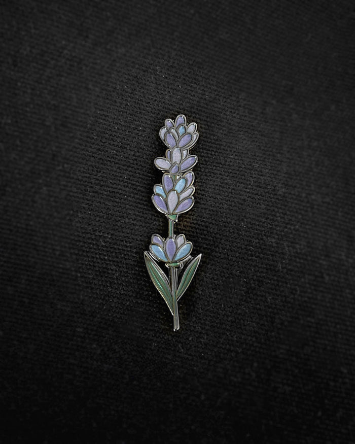 Ela Mo™ Mini Pin für Rucksäcke | Lavender. Ein kleiner Lavendel-Pin auf dem schwarzen Rucksack befestigt.