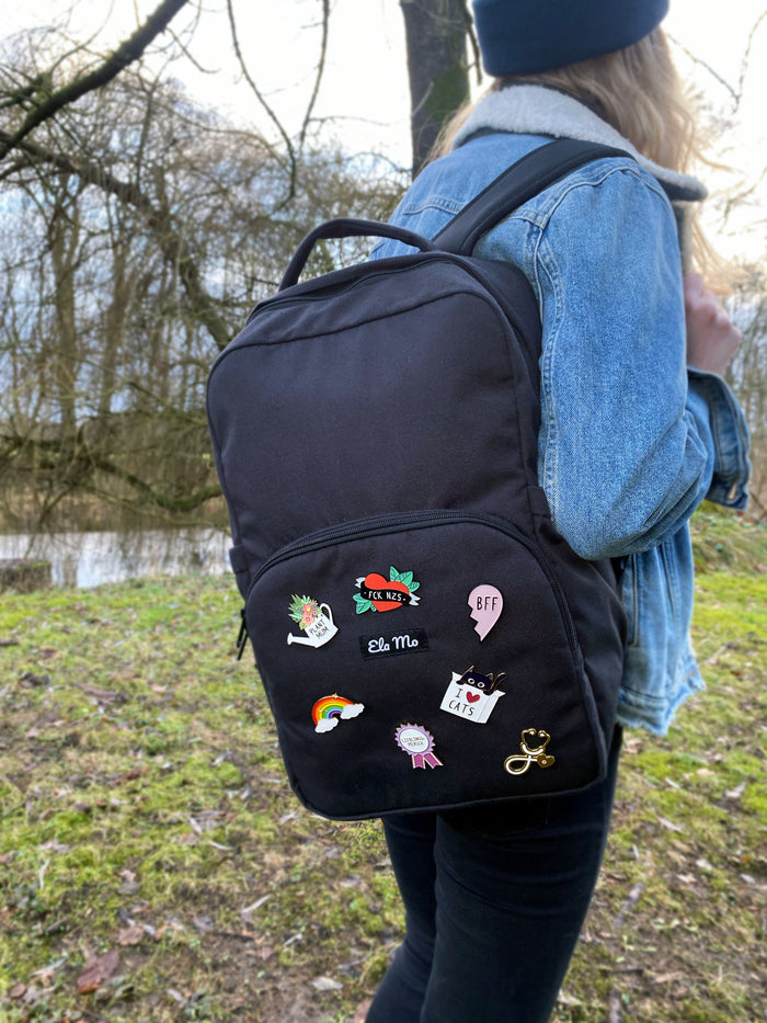 Ela Mo™ Pin für Rucksäcke| Rainbow. Eine Frau mit dem Rucksack und mehreren kleinen Pins darauf.