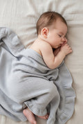 Newborn baby wrapped in a sky blue heirloom muslin ruffle blanket