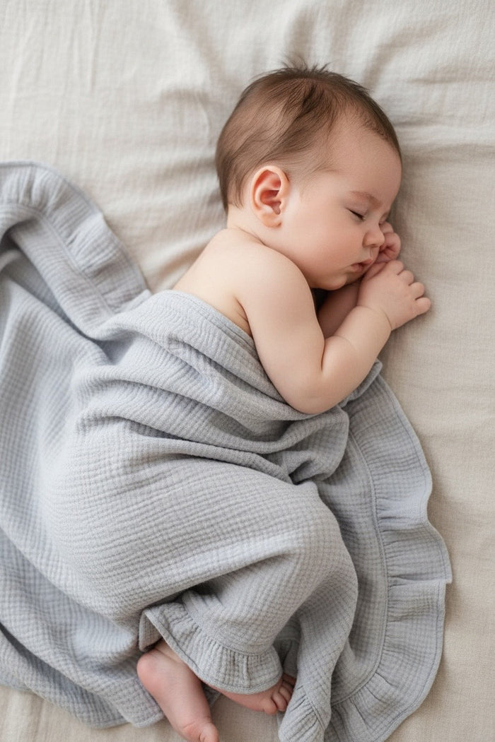 Newborn baby wrapped in a sky blue heirloom muslin ruffle blanket