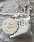 Milestone cards. Wooden 'Hello World!' disc with a drawstring bag on a textured fabric background