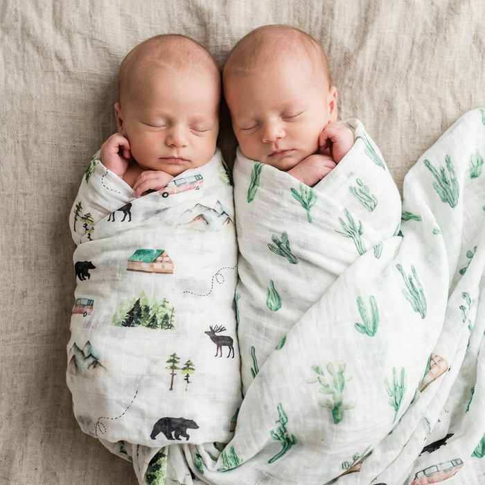 Two babies wrapped in patterned swaddles lying on a textured surface