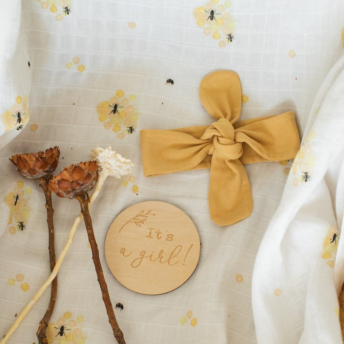 Organic cotton swaddle with jersey topknot gender reveal milestone card 'it's a girl'.
